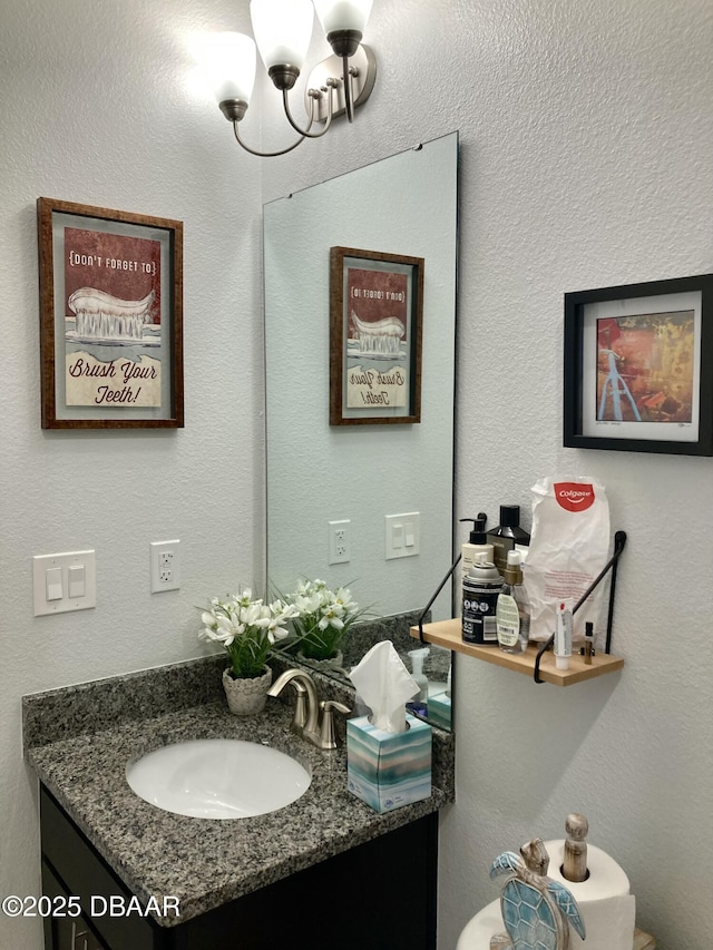 bathroom featuring a textured wall, vanity, and an inviting chandelier