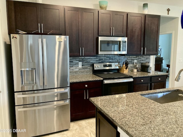 kitchen with appliances with stainless steel finishes, a sink, light stone countertops, and decorative backsplash