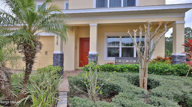 doorway to property featuring a porch, an attached garage, stone siding, and stucco siding