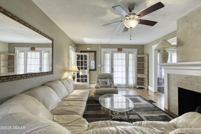 living room with a brick fireplace, ceiling fan, plenty of natural light, and wood finished floors