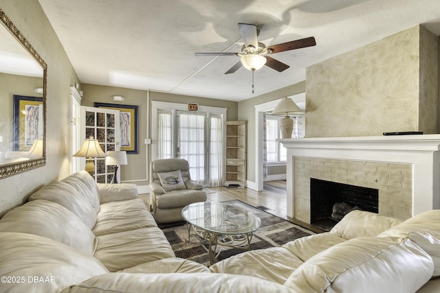 living area featuring baseboards, a ceiling fan, a brick fireplace, and wood finished floors