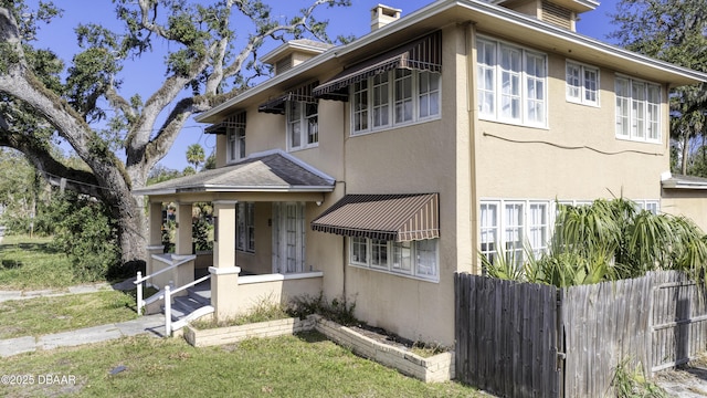 view of front of house featuring fence, stucco siding, and a chimney