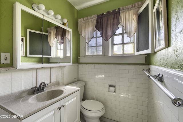 bathroom featuring toilet, tile walls, wainscoting, and vanity