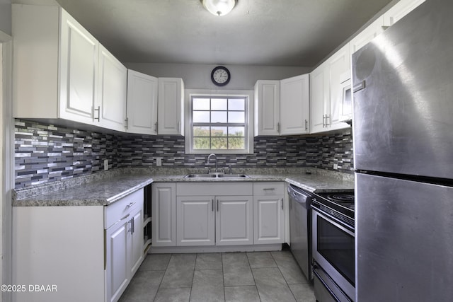 kitchen with a sink, appliances with stainless steel finishes, light tile patterned floors, and white cabinets