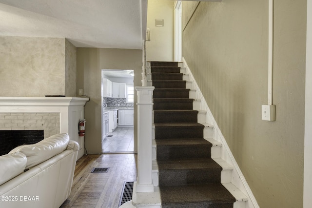staircase featuring a brick fireplace, visible vents, and wood finished floors