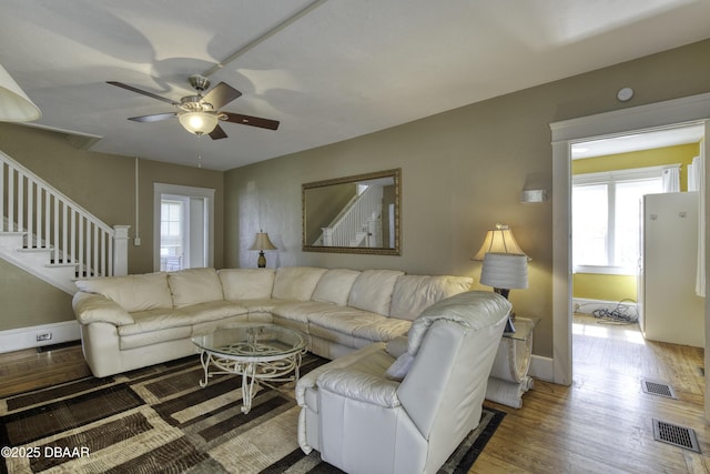 living room featuring stairs, a ceiling fan, visible vents, and wood finished floors