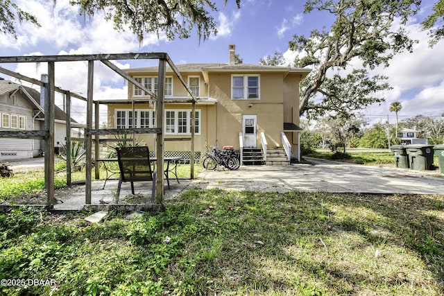 back of property featuring entry steps, a patio, stucco siding, and a chimney