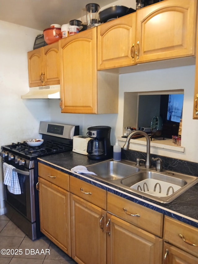 kitchen with stainless steel gas range oven, tile patterned flooring, dark countertops, under cabinet range hood, and a sink