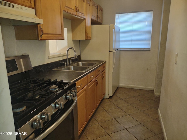 kitchen featuring dark countertops, baseboards, under cabinet range hood, stainless steel gas range, and a sink