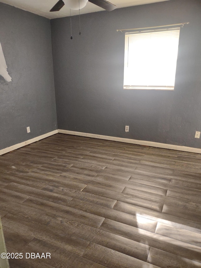 spare room with dark wood-type flooring, a ceiling fan, and baseboards