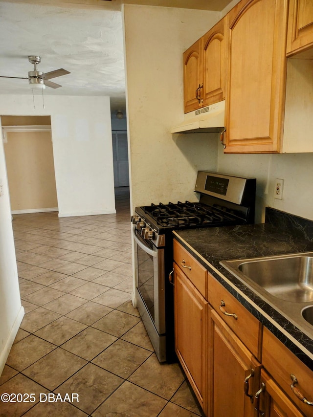 kitchen featuring under cabinet range hood, ceiling fan, a sink, dark countertops, and stainless steel range with gas stovetop