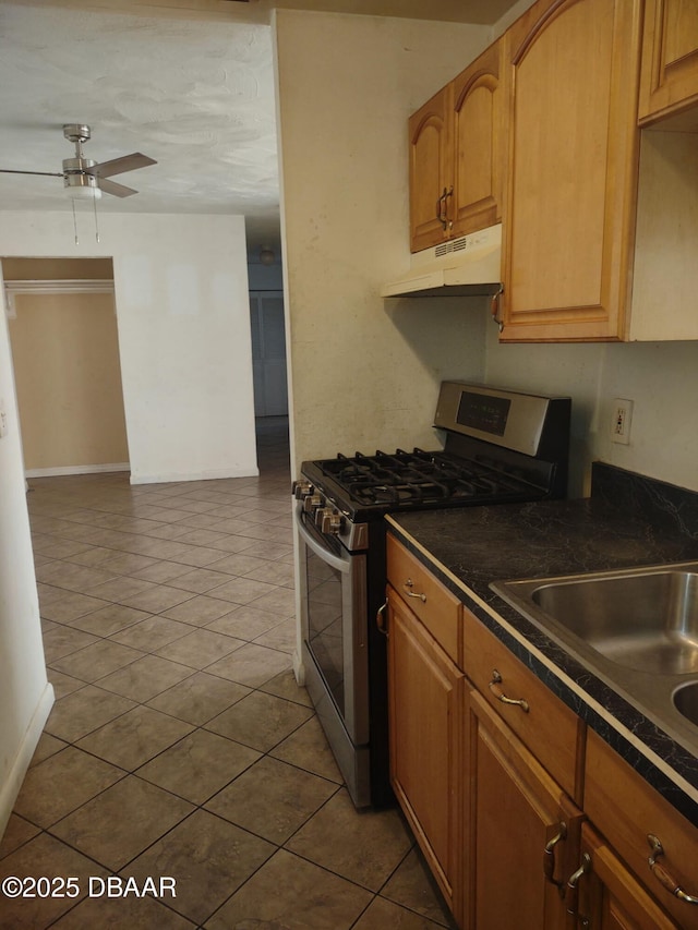 kitchen with a sink, ceiling fan, under cabinet range hood, stainless steel gas range oven, and dark countertops