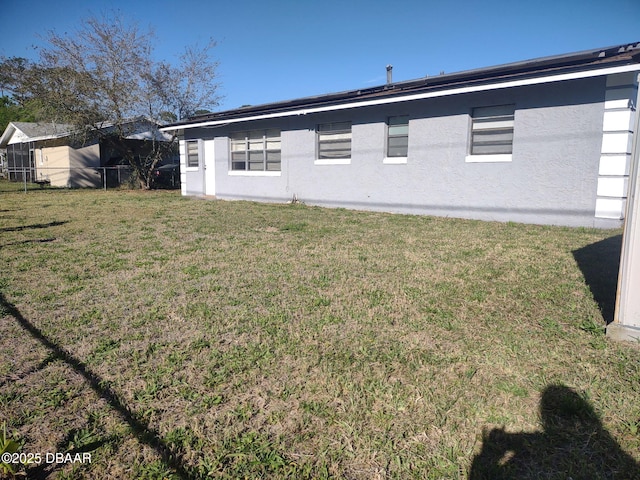 rear view of property featuring a yard, fence, and stucco siding