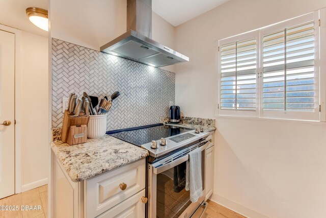 kitchen with backsplash, stainless steel range with electric cooktop, wall chimney range hood, light hardwood / wood-style floors, and light stone counters