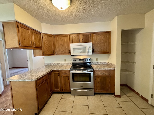 kitchen featuring brown cabinets, light countertops, white microwave, stainless steel range with electric stovetop, and a peninsula