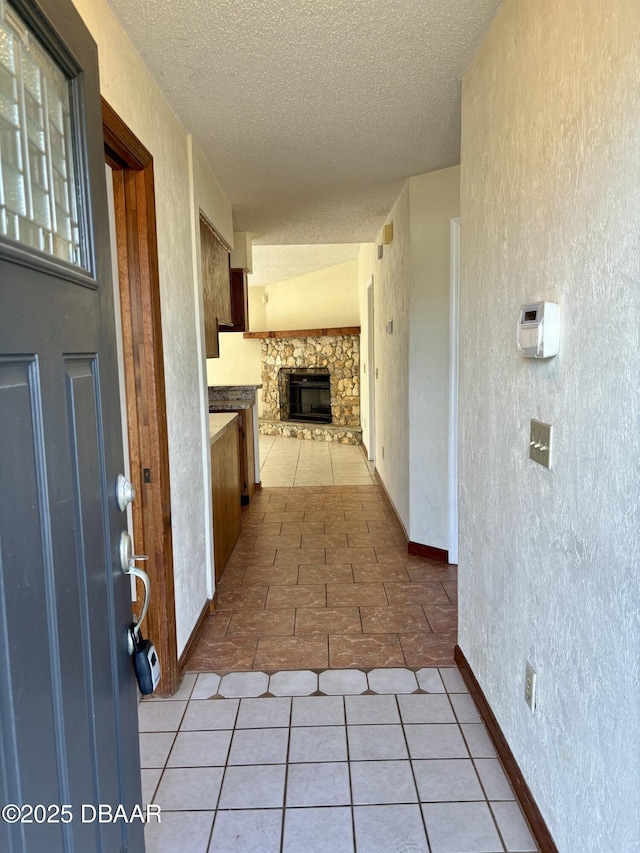 hall featuring a textured ceiling, a textured wall, light tile patterned flooring, and baseboards