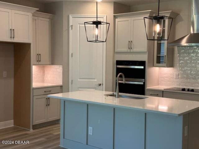 kitchen featuring tasteful backsplash, stainless steel double oven, black electric stovetop, sink, and wall chimney exhaust hood