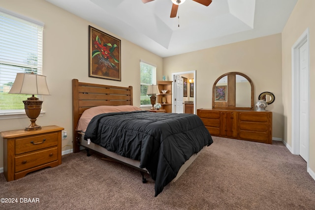 carpeted bedroom with ceiling fan, ensuite bath, and a raised ceiling