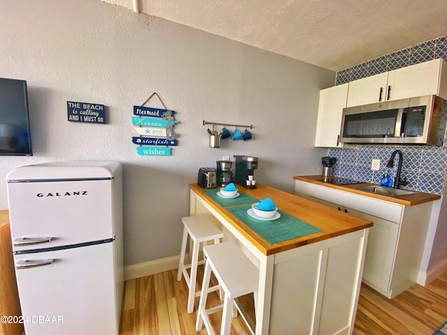 kitchen featuring butcher block counters, sink, white cabinetry, light wood-type flooring, and white refrigerator