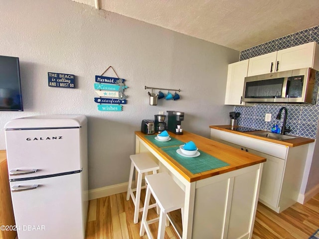 kitchen with sink, wooden counters, white refrigerator, light hardwood / wood-style floors, and white cabinets