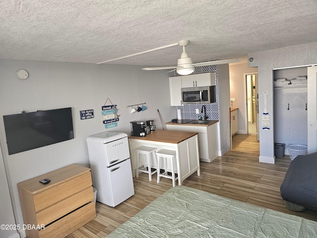 kitchen featuring a breakfast bar, refrigerator, white cabinets, ceiling fan, and backsplash