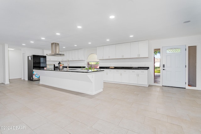 kitchen featuring white cabinetry, sink, wall chimney exhaust hood, and an island with sink