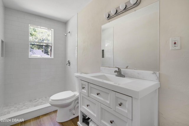 bathroom with hardwood / wood-style floors, vanity, toilet, and a tile shower