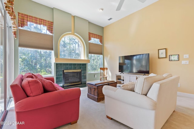 living room with ceiling fan, a high ceiling, a tiled fireplace, and light carpet