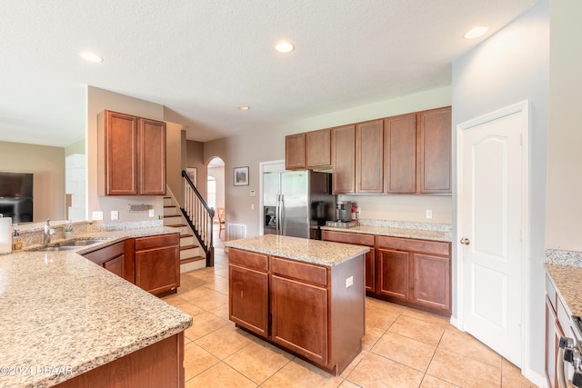 kitchen with a center island, sink, light stone counters, and stainless steel fridge with ice dispenser