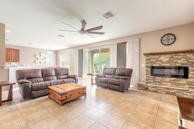 tiled living room with a textured ceiling, a fireplace, and ceiling fan