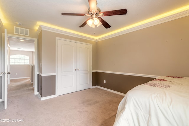 bedroom featuring ceiling fan, light carpet, a closet, and crown molding