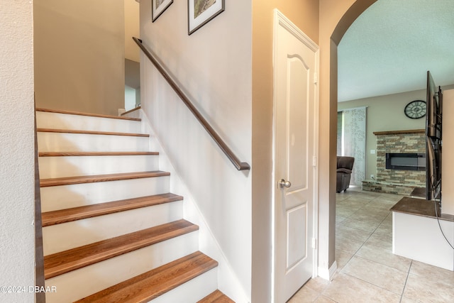 staircase with a stone fireplace, a textured ceiling, and tile patterned flooring