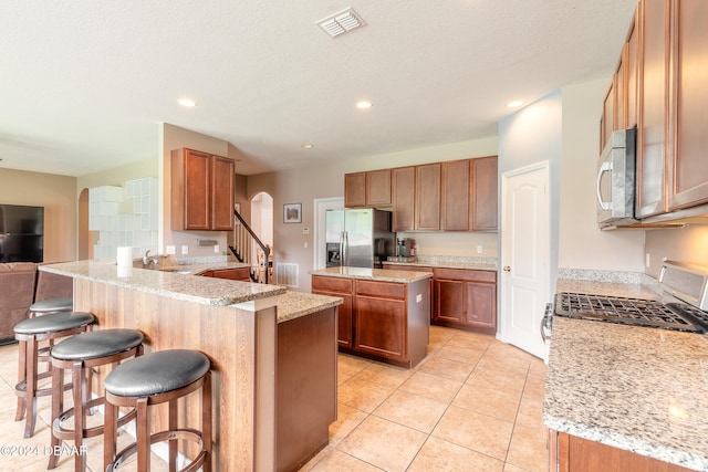 kitchen featuring kitchen peninsula, appliances with stainless steel finishes, a kitchen breakfast bar, light stone countertops, and a textured ceiling