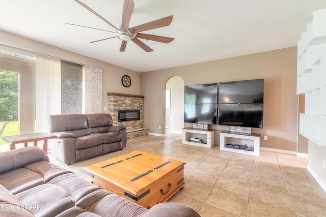 living room featuring ceiling fan, a textured ceiling, light tile patterned floors, and a stone fireplace