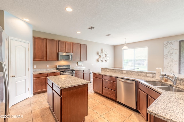 kitchen with stainless steel appliances, sink, a textured ceiling, decorative light fixtures, and a center island