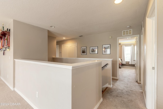 hallway with a textured ceiling and light carpet