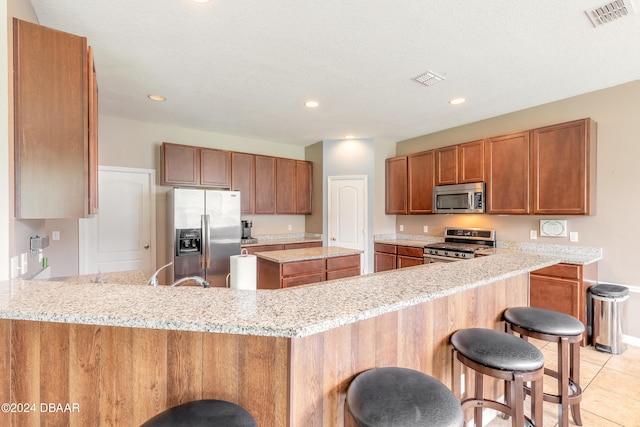 kitchen with kitchen peninsula, stainless steel appliances, light stone counters, and a kitchen breakfast bar