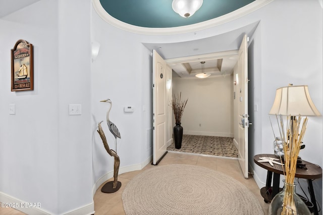 hall featuring a raised ceiling, crown molding, and light tile patterned floors