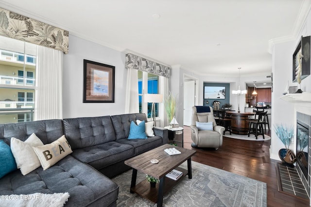 living room with a tile fireplace, ornamental molding, dark hardwood / wood-style floors, and a chandelier