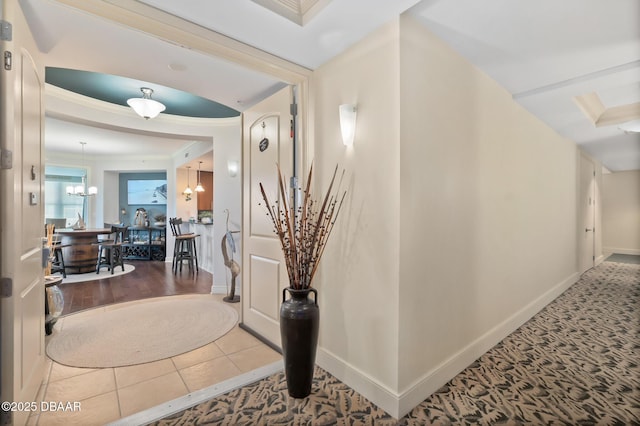 hall featuring tile patterned flooring, ornamental molding, and a notable chandelier