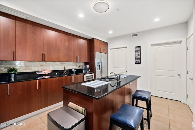 kitchen with sink, light tile patterned floors, stainless steel fridge, a kitchen island with sink, and decorative backsplash