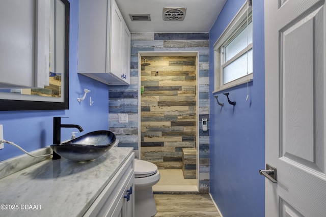 bathroom featuring vanity, wooden walls, toilet, walk in shower, and hardwood / wood-style flooring