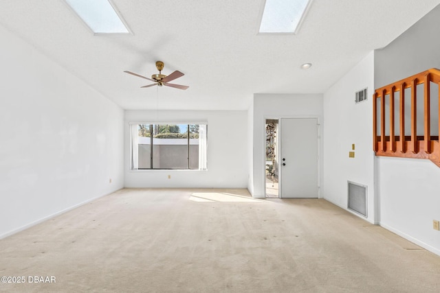 unfurnished living room with light colored carpet, a textured ceiling, and a skylight