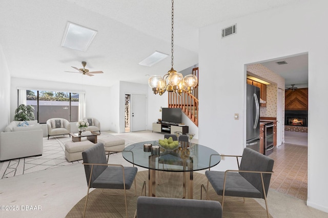 dining room featuring a textured ceiling, a fireplace, light colored carpet, and ceiling fan