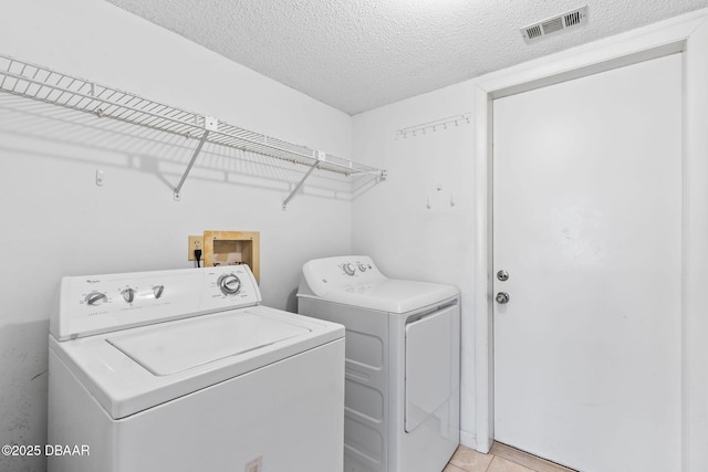 laundry room with light tile patterned floors, washing machine and clothes dryer, and a textured ceiling