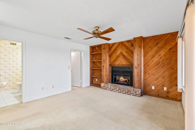 unfurnished living room with ceiling fan, wooden walls, carpet flooring, a textured ceiling, and a brick fireplace