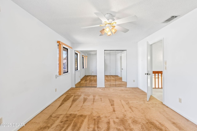 unfurnished bedroom with light carpet, two closets, a textured ceiling, and ceiling fan