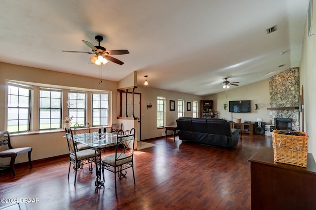 dining room with a stone fireplace, dark hardwood / wood-style flooring, lofted ceiling, and ceiling fan