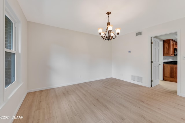 unfurnished room with a wealth of natural light, light hardwood / wood-style flooring, and a notable chandelier