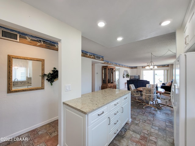 kitchen featuring light stone counters, white cabinets, a chandelier, sink, and white fridge